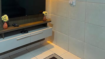 A modern living room with a flat-screen TV, a wooden entertainment unit, a vase with flowers, and a wall-mounted artwork.