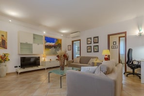 A modern living room with a flat-screen TV, a sofa, a glass coffee table, and a painting on the wall.