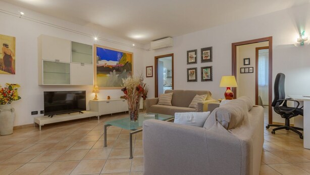 Una sala de estar moderna con televisor de pantalla plana, sofá, una mesa de centro de vidrio y un cuadro en la pared.