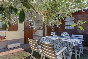 Un espace de restauration en plein air avec une table dressée pour deux personnes, entourée de chaises en bois, sous un arbre.