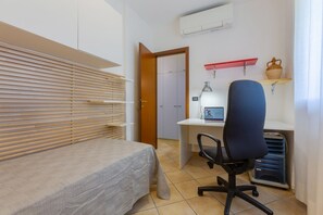 Une chambre à coucher avec un lit, un bureau avec un ordinateur, une chaise et une armoire.
