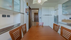 Una cocina moderna con armarios blancos, una mesa de comedor y sillas. Hay un microondas, un horno y una lámpara colgante.