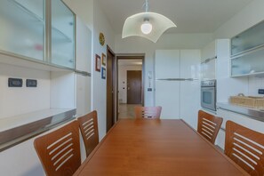 Une cuisine moderne avec des armoires blanches, une table à manger et des chaises. On y trouve un four à micro-ondes, un four traditionnel et un luminaire suspendu.