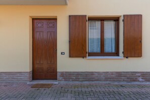 Una puerta de madera con diseños geométricos, una ventana con contraventanas de madera y un zócalo de ladrillo.