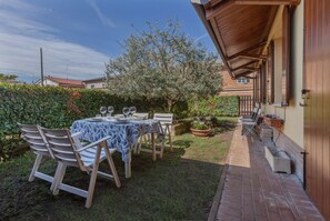 An outdoor patio with a table set for dining, surrounded by greenery and a wooden fence.