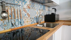 Una cocina con salpicadero de azulejos, un lavabo de acero inoxidable y una cafetera negra.
