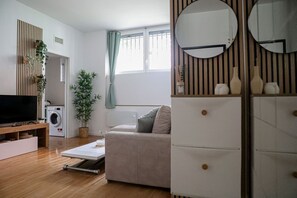 Ett modernt vardagsrum med en platt-TV, en tvättmaskin, en soffa, ett soffbord och en spegel.