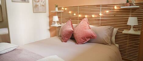 Une chambre à coucher comprenant un lit, des oreillers, des tables de chevet, des œuvres d’art murales et une tête de lit en bois agrémentée de lumières.