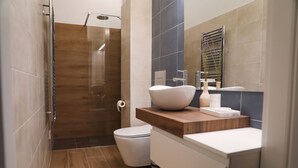 Un baño moderno con ducha, inodoro y tocador con lavamanos y espejo.