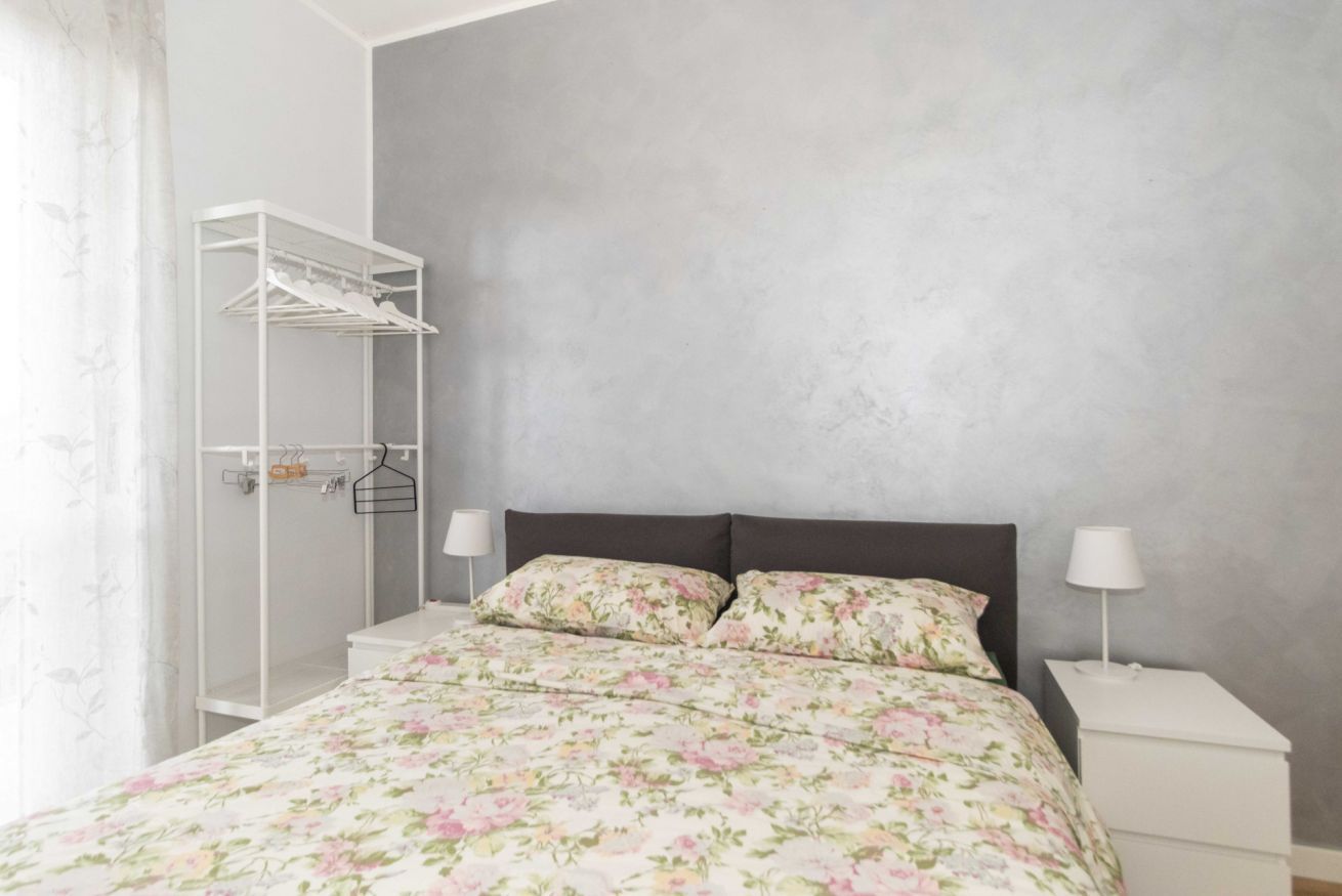 Ein Schlafzimmer mit einem Bett, zwei Nachttischen, einem weißen Kleiderschrank und einer grauen Wand.