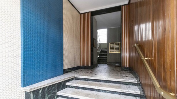 Uma escadaria leva a um quarto com porta de madeira e janela.