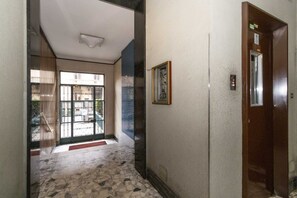 A hallway with a tiled floor, a door with an elevator, and a window with a view of the outside. - GuestHost - Cozy and spacious apartment that accommodates 4 people with great comfort, located in Vanchiglia district, at the gates of historic center, easily reachable by public transport or a 15-minute walk. The flat boasts a double exposure with a bal (Torino)