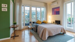 Un dormitorio con cama, escritorio, silla, televisor y balcón con vistas.