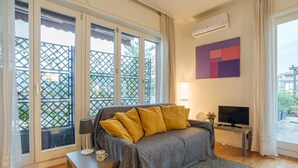 Una habitación con sofá, televisión, mesa con una taza y ventana con vista a un balcón.