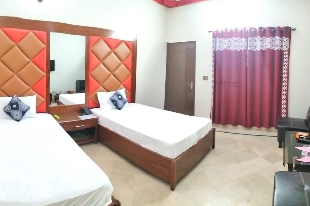 Habitación de hotel con dos camas individuales, un cabecero de madera con diseños de diamantes rojos y marrones, una mesita de noche pequeña con una lámpara y un espejo grande sobre el cabecero.