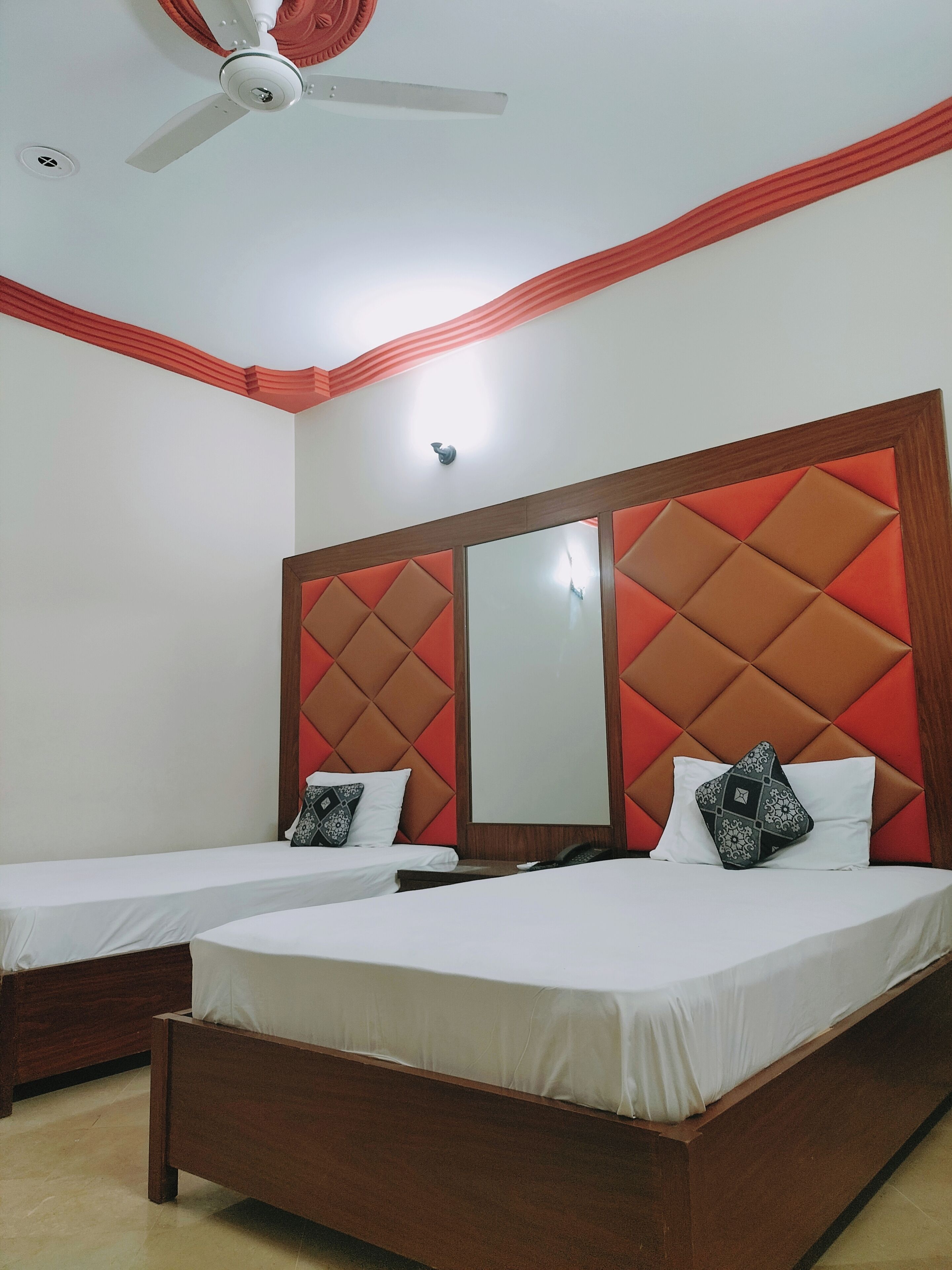 Een hotelkamer met twee eenpersoonsbedden, een plafondventilator, een wandlamp en een grote spiegel boven de bedden.