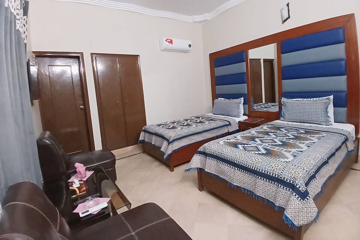Un dormitorio con dos camas, un armario de madera, una mesita con una silla y un espejo en la pared.