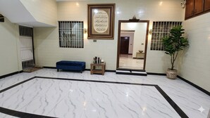 A spacious lobby with a marble floor, a blue bench, a potted plant, and a framed calligraphy piece on the wall.