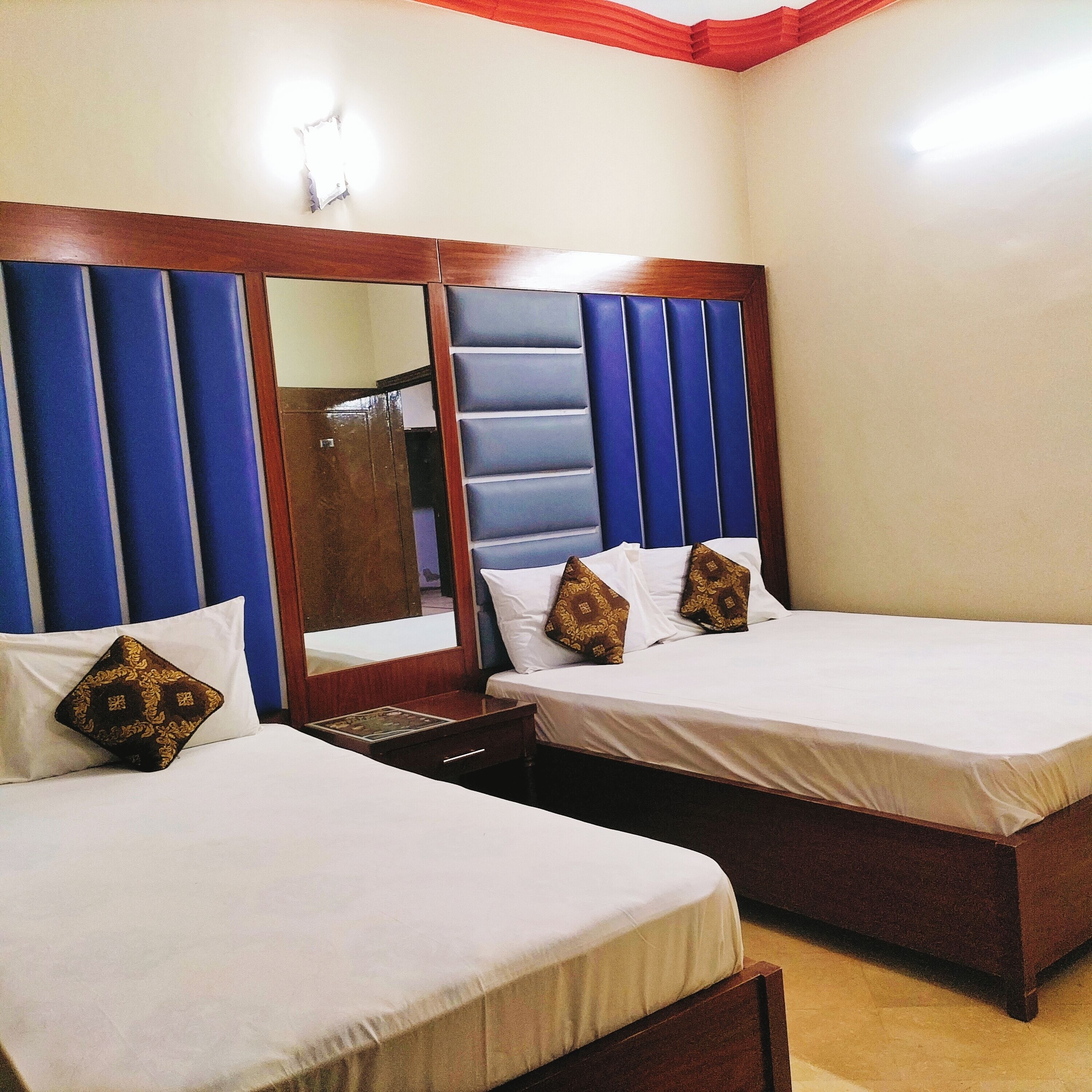 A hotel room with two single beds, a wooden headboard, a mirror, and a nightstand.