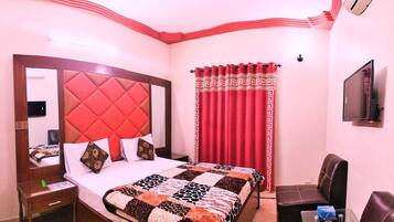 A hotel room with a large bed, a TV mounted on the wall, a red curtain, and a leather chair.