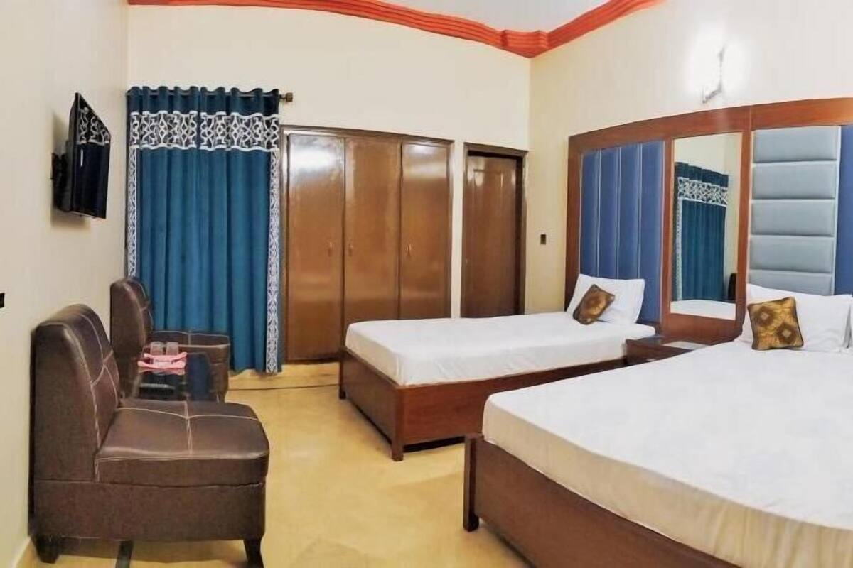 Habitación de hotel con dos camas individuales, un sofá, un armario y un televisor.