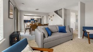 Un salon moderne avec un canapé gris, un fauteuil bleu et un poêle à bois noir.
