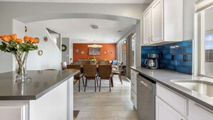 Une cuisine moderne avec des meubles blancs, un pare-feu bleu et un coin repas comprenant des chaises et une table en bois.