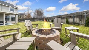 Un jardin avec un foyer en briques, entouré de fauteuils Adirondack et d’une table.