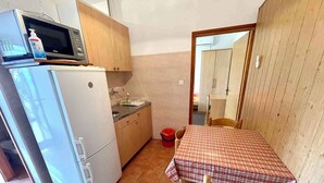 A compact kitchen with a microwave, refrigerator, sink, and a small dining table with a checkered tablecloth.
