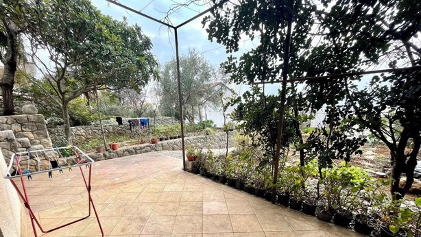 A patio area with tiled flooring, a clothes drying rack, potted plants, and a stone wall.