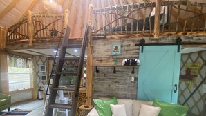 Een gezellig interieur met een houten ladder, een bank met groene kussens en een rustieke houten wand.