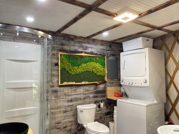 A bathroom with a toilet, a shower, a large mirror, and a wall-mounted sink.