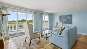 Ein geräumiges Wohnzimmer mit großem Fenster, einem Glastisch, einem hellblauen Sofa und einem weißen Sessel.
