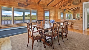 Ein Esszimmer aus Holz mit großem Tisch und Stühlen, großen Fenstern und Blick ins Freie.