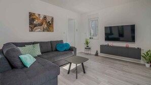 Ett modernt vardagsrum med en grå soffa, ett soffbord, en platt-TV och en minimalistisk design.