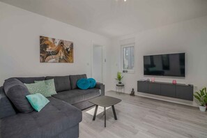Ein modernes Wohnzimmer mit grauem Sofa, Couchtisch, Flachbildfernseher und minimalistischem Design.