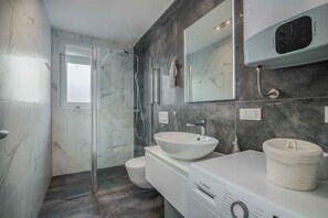 Un bagno moderno con cabina doccia in vetro, lavabo bianco e lavatrice Bosch.