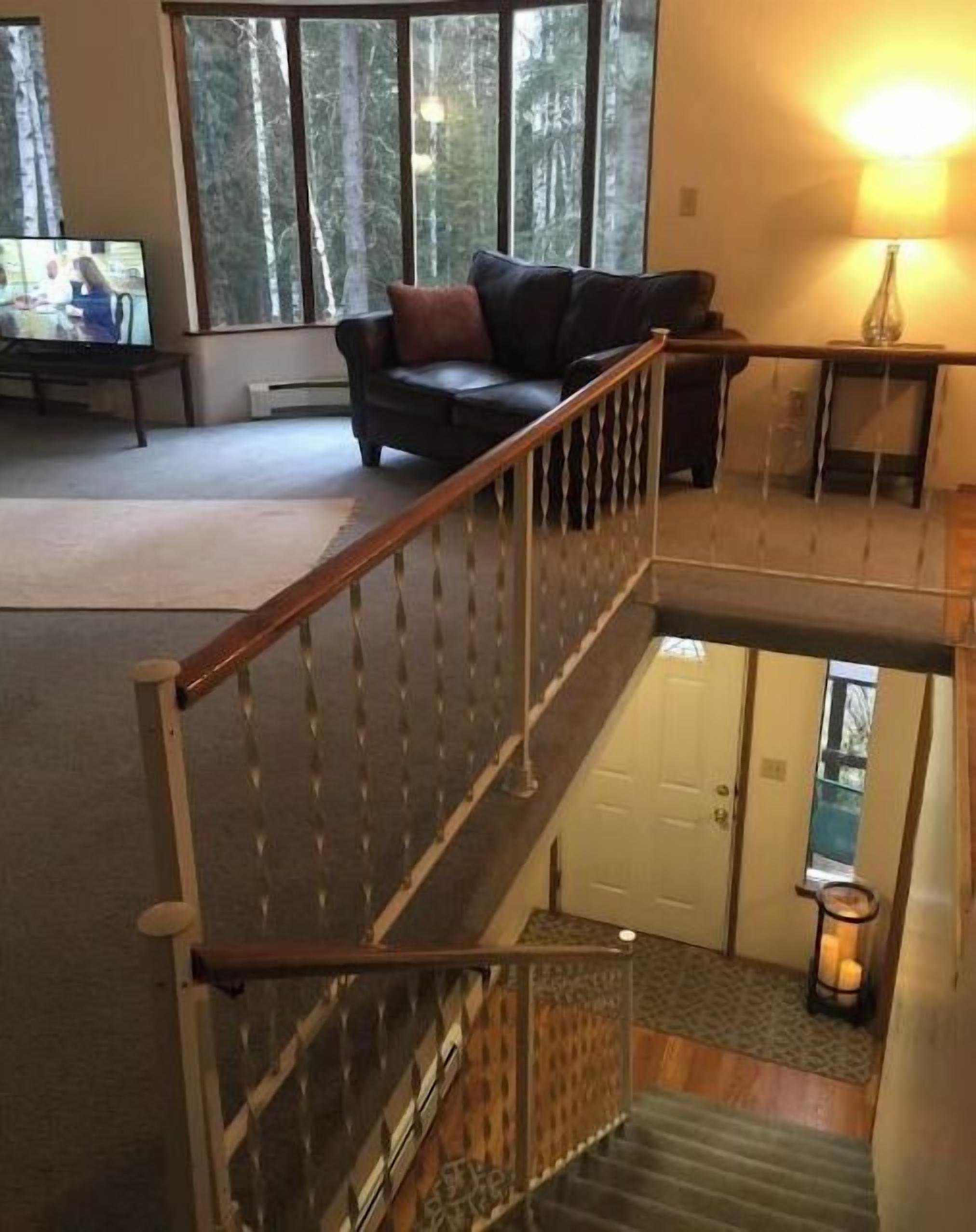 A multi-level interior with a staircase, a sofa, and a view of trees through large windows.
