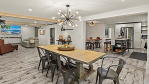 Un amplio espacio de sala de estar con un gran comedor de madera, luminarias modernas y una cocina equipada con electrodomésticos de acero inoxidable.