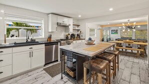Una cocina moderna con gabinetes blancos, electrodomésticos de acero inoxidable y una isla central con taburetes.