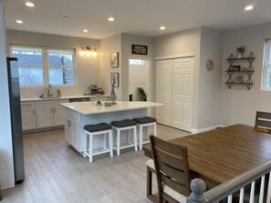 A modern kitchen with white cabinetry, a central island with bar stools, a dining table with chairs, and a built-in oven.