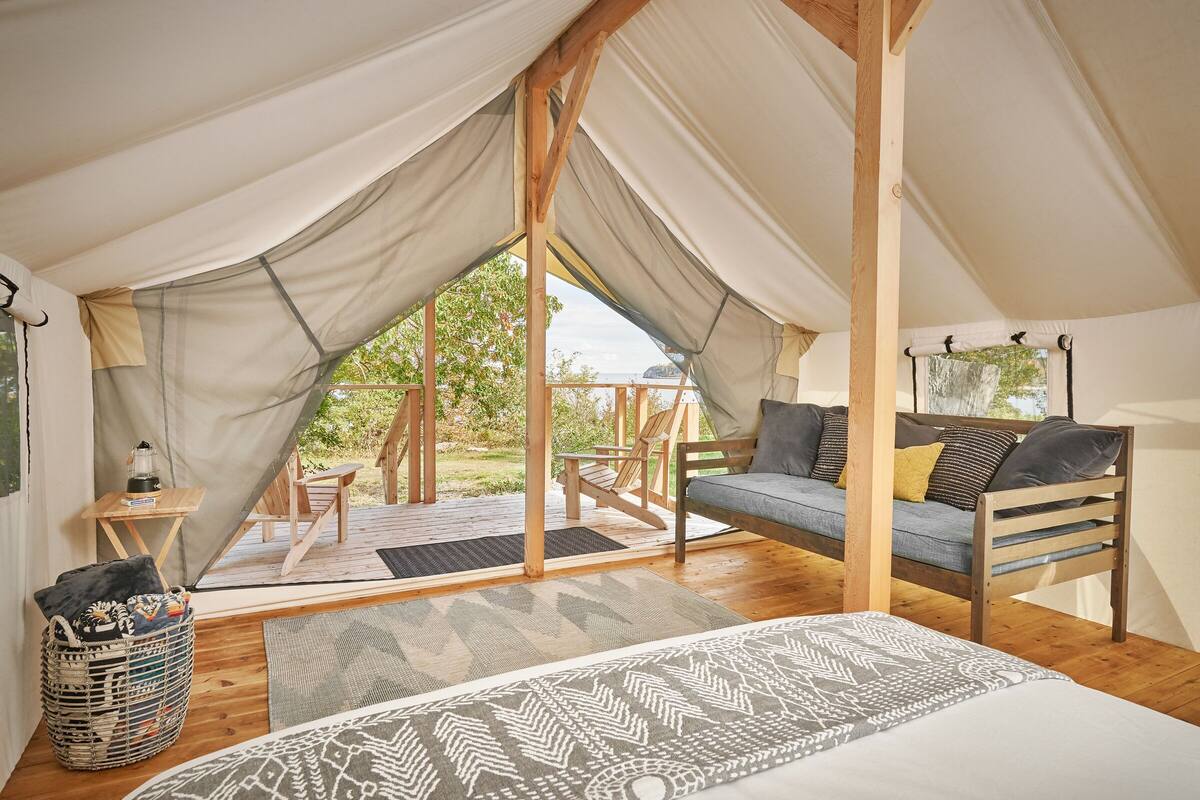 A tented accommodation with a bed, a sofa, and a table with a lantern.