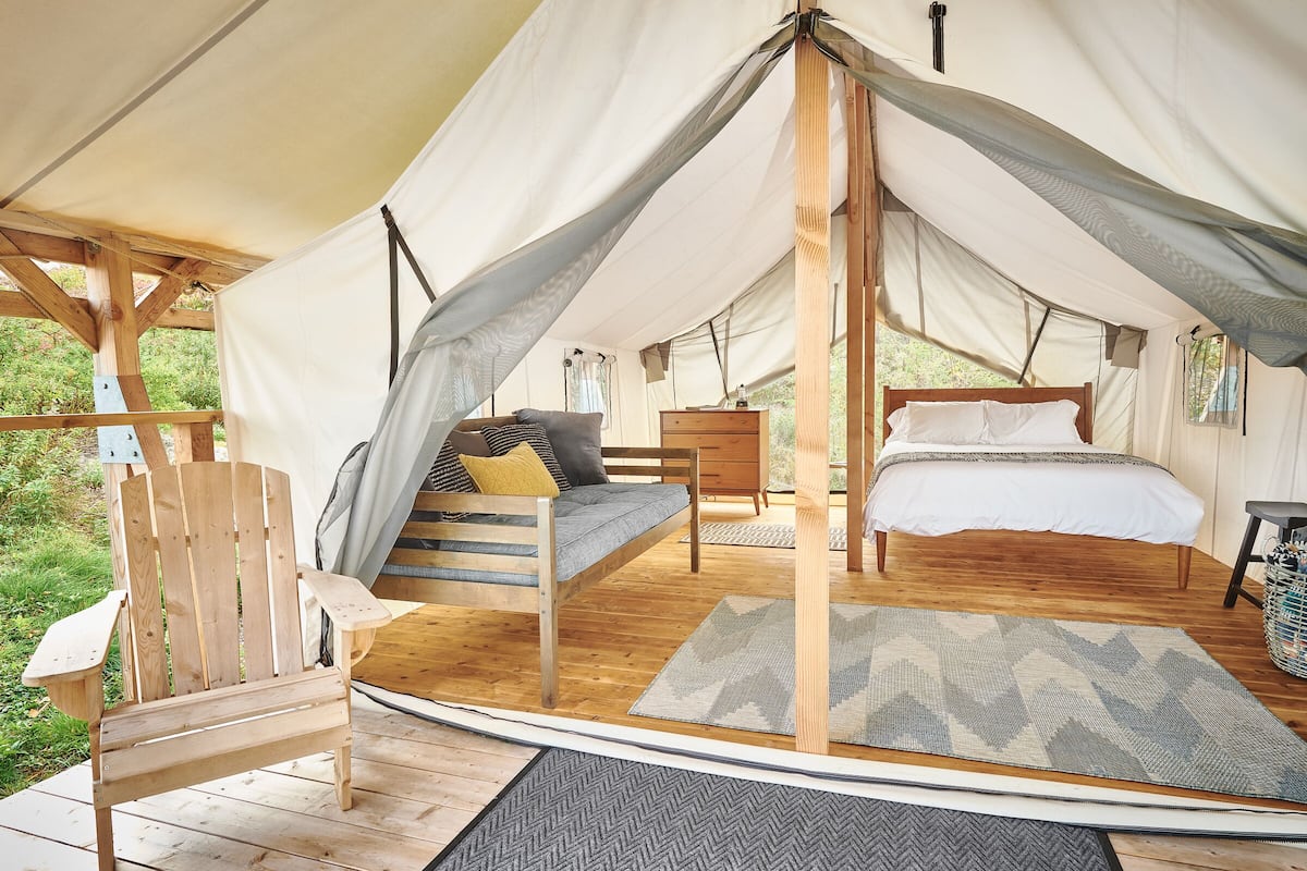 A tented accommodation with a wooden bed, a sofa, and a chair.