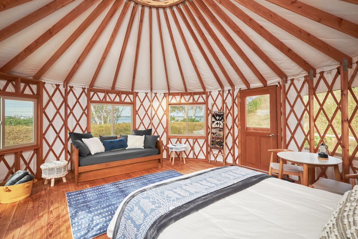 A yurt with a wooden interior, a sofa, a bed, a small table, and a window.