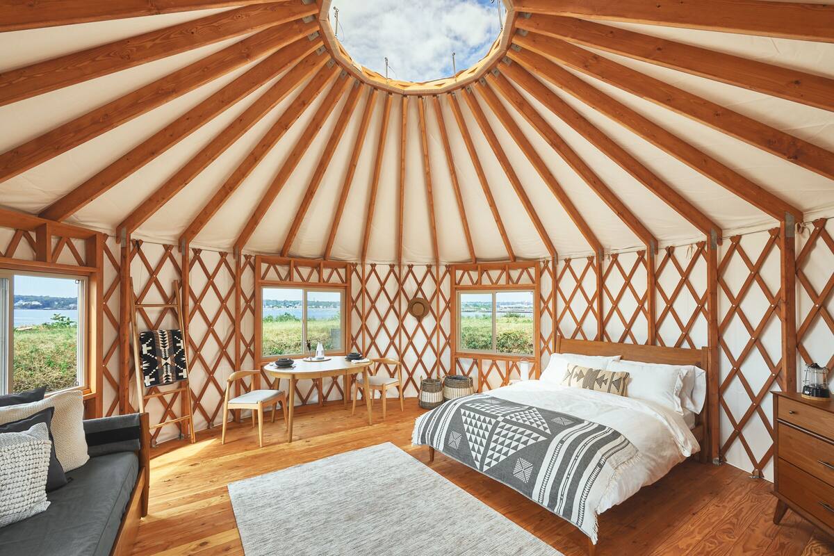 A yurt with a bed, a desk, and a view of the outdoors.