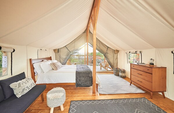 A tented accommodation with a bed, sofa, and wooden dresser. - Fortland Island Campground (Portland)