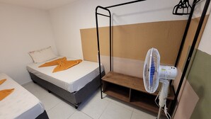 A small, clean room with two beds, a standing fan, and a wooden bench. - Self Hostel (São Paulo)