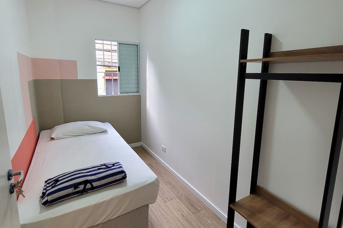Una habitación pequeña y limpia con cama, ventana y litera.