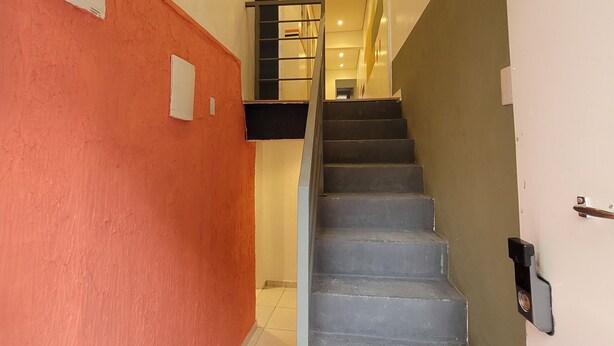 A staircase with a metal handrail leading to a landing. - Self Hostel (São Paulo)
