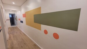 A hallway with a wooden floor, a door at the end, and a wall with abstract geometric shapes. - Self Hostel (São Paulo)